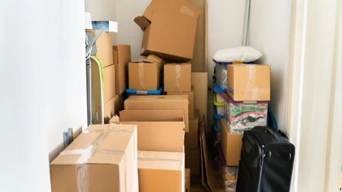 Cardboard boxes stacked on plastic totes in a room with luggage